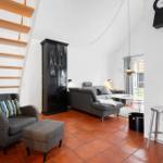 Living room with gray sofa, wooden staircase, and terracotta floor