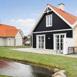 Black wooden house with red roof and white trim, beside yellow house and green areas.