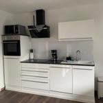 Moderne Küche mit weißen Schränken, schwarzer Arbeitsplatte und integriertem Ofen.