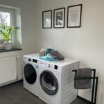 Wäscherei mit Waschmaschine und Trockner, Fenster mit Pflanze und Dekoration.