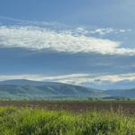 Weitläufige Landschaft mit grünen Hügeln und blauem Himmel mit weißen Wolken.