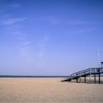 Strand mit Rettungshütte und Holzsteg. Klare blaue Himmel über dem Meer.