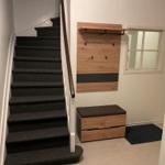 Treppe mit Holzgeländer, Wandregal und Sitzbank im Eingangsbereich.