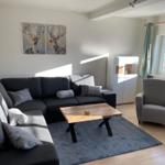 Wohnzimmer mit Sofa, Sessel und Tisch. Wandbild mit Hirsch. Fenster mit Vorhängen.