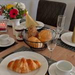 Frühstückstisch mit Croissant, Brot, Marmelade und Blumen.