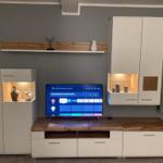 TV-Gerät auf Holzkonsole mit weißen Schränken und beleuchteten Nischen.