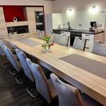 Langes Esszimmer mit Holztisch und Stühlen, Küche im Hintergrund.