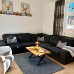 Ein Wohnzimmer mit schwarzer Couch, Holztisch und Fensterblick.