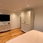 Schlafzimmer mit Bett, Kleiderschrank und Fernseher an der Wand.