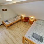 Zimmer mit zwei Betten, Holzboden und roter Sitzgelegenheit.