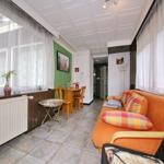 Wohnzimmer mit orangefarbenem Sofa, Tisch und Stühlen, Fenster mit Vorhängen und Kachelboden.