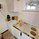 Küche mit Spüle, Herd, Mikrowelle und Fenster mit Blumen.