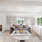 Wohnzimmer mit grauem Sofa, Glas-Tisch und Fenstern mit Blick auf Garten.