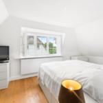 Schlafzimmer mit Dachfenster, Bett, Fernseher und Holzboden.