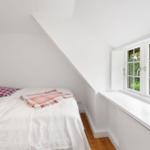 Schlafzimmer mit Dachschräge, Bett und Fenster mit Blick auf Grün.