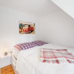 Schlafzimmer mit Bett, Kissen und Decke. Wandbild zeigt einen VW-Bus.