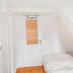 Schlafzimmer mit Dachschrägen, Bett und Tür mit getöntem Glas.