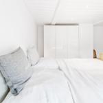 Schlafzimmer mit weißem Bett, grauem Kissen und weißen Wänden.