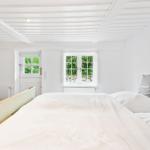 Schlafzimmer mit weißer Wand und Bett. Fenster und Tür zeigen grüne Außenansicht.