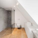 Badezimmer mit Dusche, Toilette und Waschbecken unter Dachschräge.