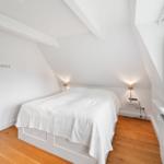 Schlafzimmer mit Dachschrägen, weißem Bett und Holzboden
