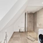 Badezimmer mit Dusche, Toilette und Waschmaschine unter Dachschrägen.