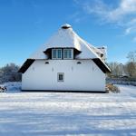 Schneebedecktes Haus mit strohgedecktem Dach und weißen Wänden.