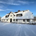 Schneebedecktes Haus mit strohgedecktem Dach und weißen Wänden.