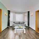 Wohnzimmer mit Sofa, Glas-Tisch und Blick auf Balkon. Nebenraum mit Dusche und Toilette.