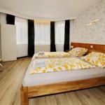 Zimmer mit Doppelbett, Holzboden und Fenstern mit Vorhängen.