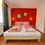 Schlafzimmer mit Doppelbett, roter Wand und Fenster mit Vorhängen.