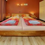 Zwei Betten mit bunten Bettwäsche und Holzrahmen. Wandbeleuchtung und Kleiderschrank.