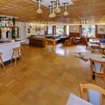 Großer Raum mit Holzboden, Tischen, Stühlen und Bar. Decke mit Holzverkleidung und Lampen.