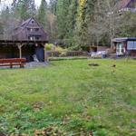 Grüner Garten mit Holzveranda, Terrasse und kleinem Haus im Hintergrund.