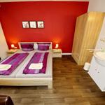 Schlafzimmer mit Doppelbett, roter Wand und integriertem Bad.