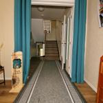 Hausflur mit Teppich, blauen Vorhängen und Holzschrank. Treppenhaus im Hintergrund.