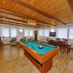 Raum mit Billardtisch, Esstisch und Sitzgelegenheiten unter Holzdecke.