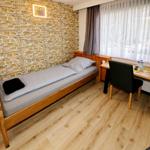 Ein Zimmer mit Holzbett, Schreibtisch und Steinwand. Fenster mit Vorhängen.