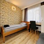 Ein Schlafzimmer mit Holzbett, Schrank und Schreibtisch an Fenster