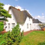 Weiße Hütte mit Strohdach, Garten und Liegestühle.