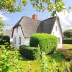 Haus mit Strohdach und gepflegtem Garten. Grüne Hecken und Rasenfläche.
