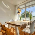 Esszimmer mit Holztisch, weißen Stühlen und großem Fenster mit Blick auf Grün.