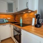 Küche mit Holz Arbeitsplatte, weißen Schränken und Edelstahl Kochfeld.