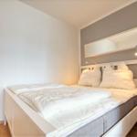 Schlafzimmer mit weißem Bett, Spiegelschrank und Nachttisch.