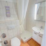 Badezimmer mit Dusche, Waschbecken und Toilette. Fliesenboden und Spiegelschrank.