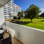 Balkon mit Tisch und Stühlen, Blick auf Grünfläche und Gebäude.
