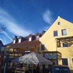 Gelbes Gebäude mit Dachgauben und Terrasse unter blauem Himmel.