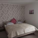 Schlafzimmer mit Bett, Kopfkissen, Wandverkleidung und Kleiderständer.