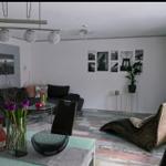 Wohnzimmer mit Sofa, Sessel und Glas-Tisch. Wand mit Bildern und Pflanze.