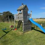 Holzspielplatz mit Rutsche und Schaukel auf grünem Rasen.
